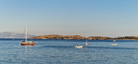 A peaceful coastal scene featuring a large sailboat and several smaller boats on calm blue water. A...
