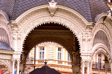 This is a detailed shot of the Mill Colonnade in Karlovy Vary. The photo focuses on the intricate, ornate arches and decorative carvings of the Neoclassical building, with another building visible through the main arch.の写真素材
