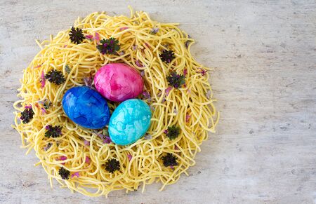 concept and idea Easter eggs in a nest of egg noodles on a light colored wood table. copy space room...