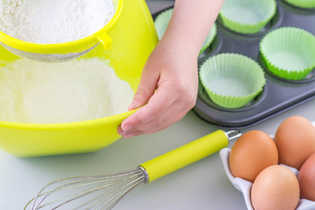 Child sieving flour into a bowl in preparation for cooking cake, room for text
