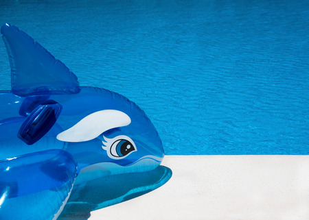 Pool side background shot on a sunny summers day showing an inflatable dolphin resting on a marble...