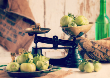 authentic spanish farmhouse scene showing freshly picked organic green tomatoes in green scales on an old wooden table , soft window light.filter added for moodの写真素材