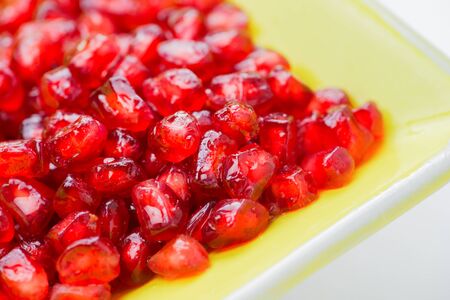  rich red pomegranate seeds washed in a yellow dish blurred background fro copy space 