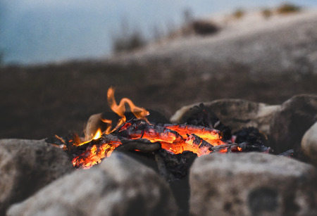 campfire in the wilderness while camping  blue lake in the distance selective focus on the embers blurred background  to ad copy space の写真素材