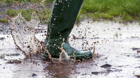 child jumping in a wet muddy puddle  with green wellington  boots  in the early morning light  copy space to side of imageの写真素材
