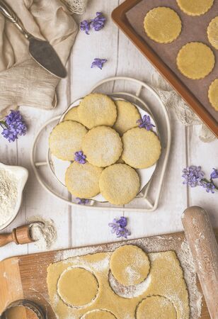 Top view of plate with freshly baked aromatic cookies on white wooden table with raw dough and cutters in flourの写真素材