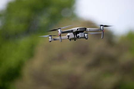 Contemporary drone with camera facing down exploring countryside while flying on blurred background of green hill in summer in natureのeditorial素材