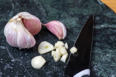 From above sharp knife and pieces of garlic with cloves  placed on marble table near unpeeled clovesの写真素材