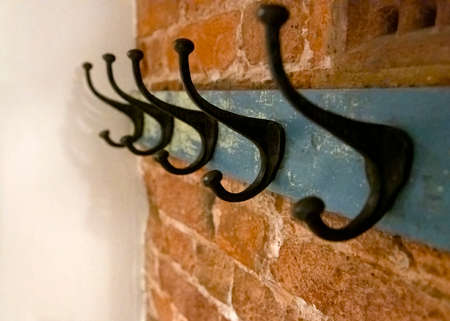 Wrought iron coat hangers place on old blue vintage wood hung on a brick textured wall with a blank...