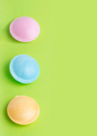 Colorful flying saucer candy in pink, blue, and yellow are aligned vertically on a green background, showcasing vibrant and playful confectionery in a minimalist composition.の写真素材
