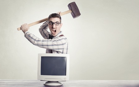 young angry nerd destroying old computer monitor.