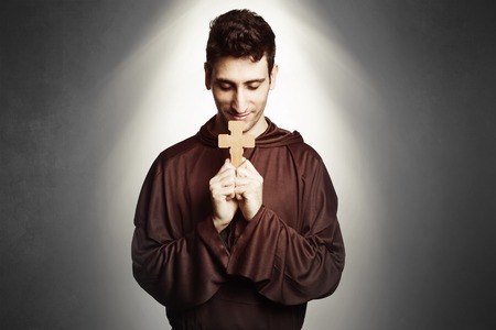 young friar with habit praying on background.