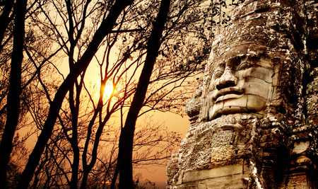 Giant stone face in Prasat Bayon Temple and trees on sunset sky background. Famous landmark Angkor Wat complex, khmer culture, Siem Reap, Cambodiaの写真素材