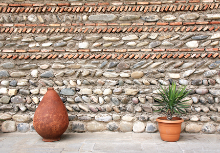 Clay jug, flowerpot with green palnts and ancient wall, Georgiaの写真素材