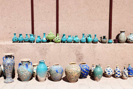 Traditional iranian souvenirs - colorful clay pot and jug, Yazd, Iran. Clay jugs of various shapes of green and blue colors on a shelf near the adobe wall. Copy space for textの写真素材