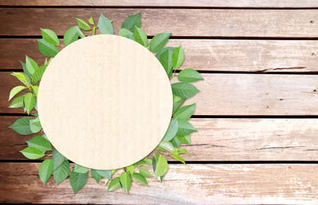 Green leaves and round paper card on wood texture. Horizontal banner with eco paper texture. Wooden planks, recycled carton material label and green leaf. Copy space for text. Mock up templateの写真素材