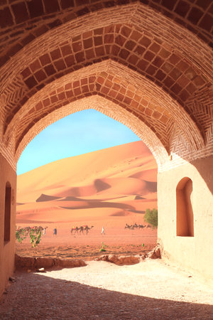 Ancient arch at the entrance to desert. View of sand dunes through stone arch. Travel, resort, vacation and holiday concept. Beautiful desert landscape with sand dunes and camelsの写真素材