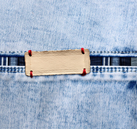 Blue denim texture with a seam and paper label. Light blue color denim jeans fabric and vintage paper tag. Mock up template. Copy space for textの写真素材