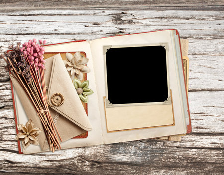 Retro book with photo, dry leaf, vintage envelope and paper card on old wooden board. Nostalgic scrapbooking backdrop. Mockup template. Copy space for textの写真素材