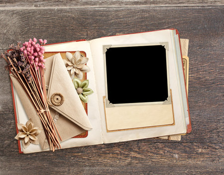Retro book with photo, dry leaf, vintage envelope and paper card on old wooden board. Nostalgic scrapbooking backdrop. Mockup template. Copy space for textの写真素材