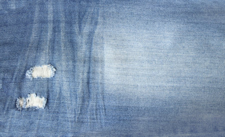 Ripped jeans material of indigo color. Horizontal or vertical background with denim texture of blue color with torn holesの写真素材
