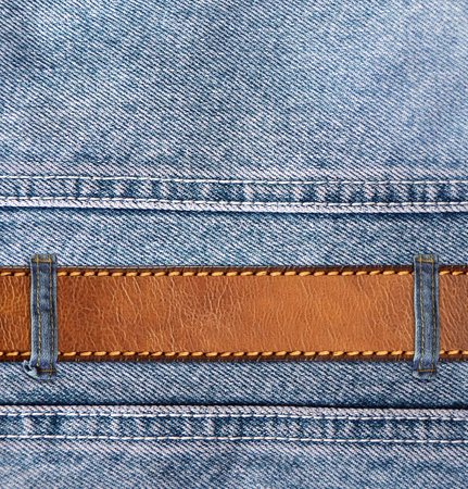 Blue denim background with leather belt. Horizontal or vertical backdrop with light blue color denim jeans fabric texture and brown leather strap. Mock up template. Copy space for textの写真素材