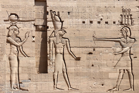 Ancient Egyptian bas-relief on stone wall with figures of the goddess Isis, the god Horus and Pharaoh. Temple of Isis on Agilkia Island (Philae), reservoir of Aswan Low Dam, Egyptの写真素材