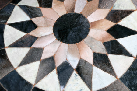 Rounded Handmade Cowhide Fur Carpet in patchwork style. Detail of stitched together fur blocks of brown, beige and dark brown colors. Homemade round leather rug carpetの写真素材