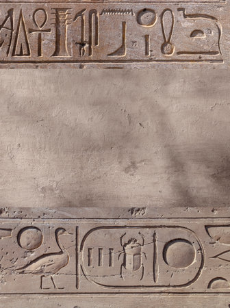 Vertical background with ancient Egyptian hieroglyphs on stone wall, Egypt, Africa. Backdrop with sandstone carving with hieroglyph. Mock up template. Copy space for textの写真素材