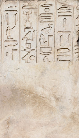 Vertical background with ancient Egyptian hieroglyphs on stone wall, Egypt, Africa. Backdrop with sandstone carving with hieroglyph. Mock up template. Copy space for textの写真素材