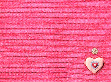 Wool sweater texture of red color, button and felt heart. Horizontal background with natural knitted wool material. Valentine's day backdrop heart-shaped patch label. Copy space for textの写真素材