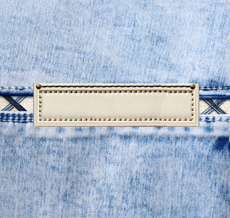 Blue denim texture with a seam and old leather label. Light blue color denim jeans material and vintage tag of ivory color. Mock up template. Copy space for textの写真素材