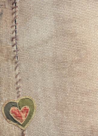 Two pieces of old burlap sewn together with thread and fabric heart. Vertical background with rustic bag texture and Valentine's day decor in patchwork style. Copy space for textの写真素材