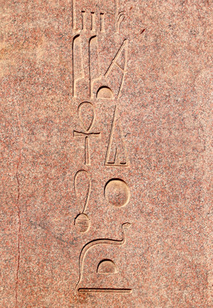 Vertical background with ancient Egyptian hieroglyphs on red granite wall, Egypt, Africa. Backdrop with granite carving with hieroglyph. Copy space for textの写真素材