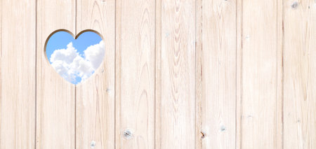 Heart-shaped hole in wooden boards and blue sky with clouds. Heart shape hole in wood fence. Go green. Ecology, global ecological resource, eco and zero waste concept. Copy space for textの写真素材