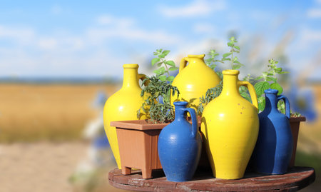 Rustic clay jugs of yellow and blue colors on wooden table on sunny nature background. Colourful traditional decorative jugs for wine on blurred backdrop of the countrysideの写真素材