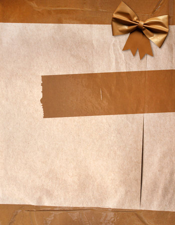 Paper package covered in adhesive tape with decorative bow. Masking tape with paper. Vintage grunge adhesive tape strips and bow on old cardboard texture of brown color. Copy space for textの写真素材