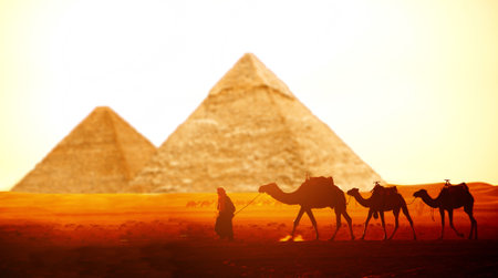 Horizontal banner with caravan of camels and Great Pyramids of Chephren and Cheops, Cairo, Egypt. Man with three dromedary in two pyramids, Giza complex (Giza Necropolis). On sunrise sky backgroundの写真素材