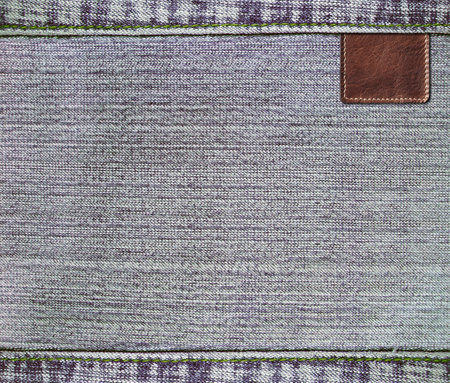 Grey denim texture with a seam and old leather label. Light gray color denim jeans material and vintage tag of brown color. Mock up template. Copy space for textの写真素材