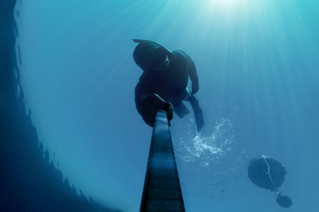Freediver holding his breath deap in the water with Sunlight above him.の写真素材