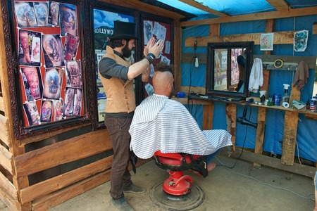 CHERNIVTSI, UKRAINE - JULY 22, 2017: Stylish hairdresser in the cylinder cap Shears and shaves a biker with red hair at the festival Moto-picnic Retrodrom 2017のeditorial素材