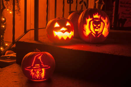 3 carved pumpkins sit on the steps of a home on the night of halloweenの写真素材