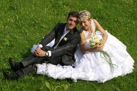 Beautiful newly-married couple sit on a grassの写真素材