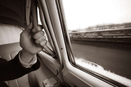 The man's hand keeps for the handle of the automobile. b/w+sepia