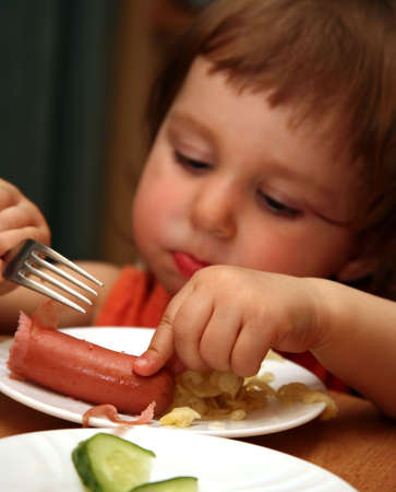 The small child eats sausage with macaroni. The foreground in a zone of sharpness, the rest is dimの写真素材
