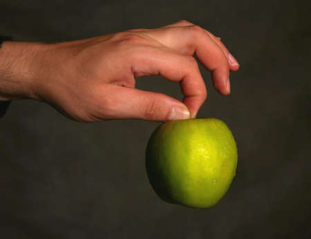Man's hand with a green apple on a dark background