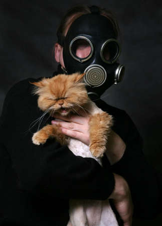 The man in a gas mask holds a shouting red catの写真素材
