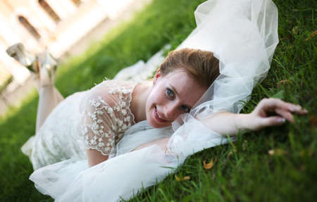 The beautiful bride with a wedding bouquet lays on a grassの写真素材