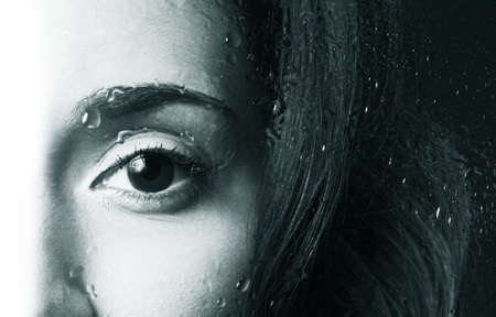 The beautiful girl behind wet glass