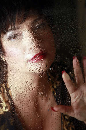 Portrait of the beautiful brunette behind a wet windowの写真素材